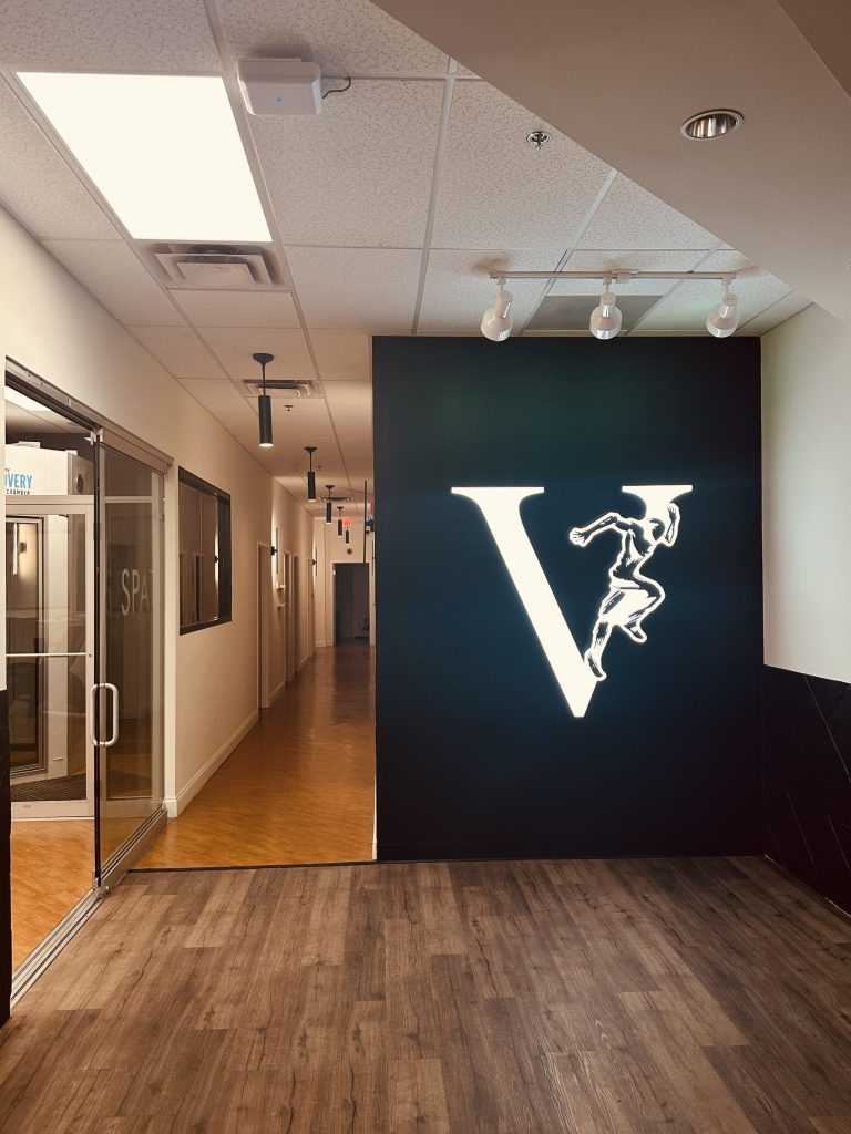 Recovery and spa hallway beneath the lit Club Five V at Club Five Health in Libertyville, IL